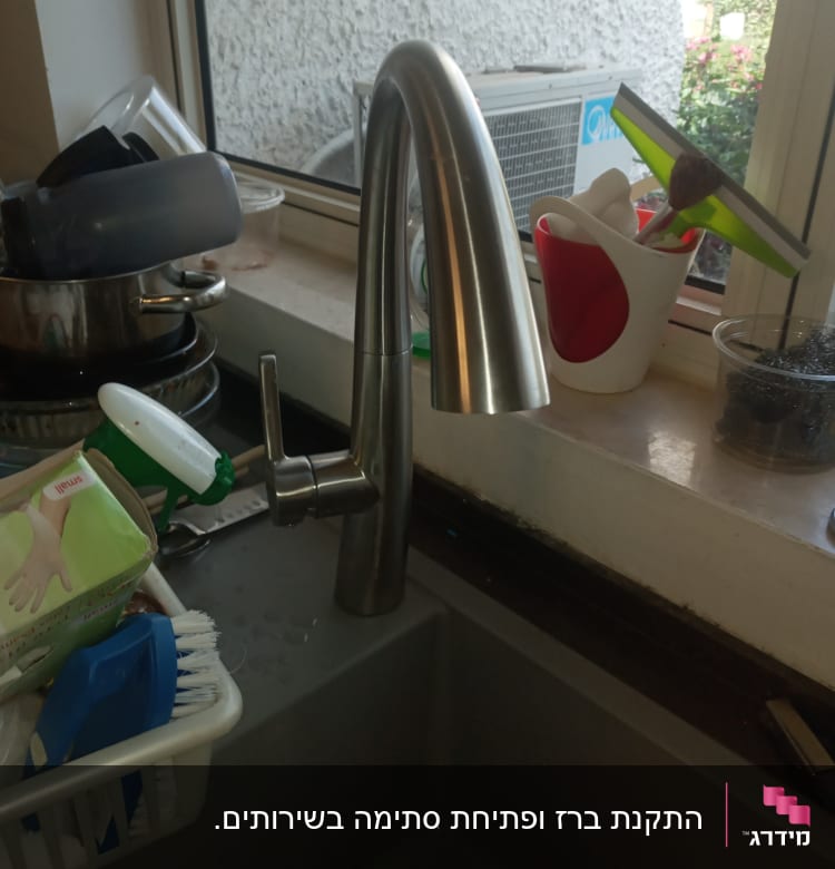 ברז נירוסטה בכיור מטבח עם כלים מסביב
